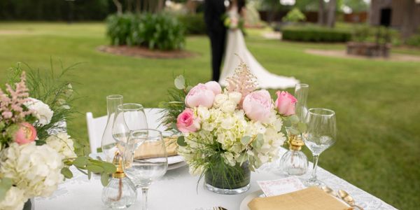Elegant floral centerpiece on a wedding table with a bride and groom in the background.