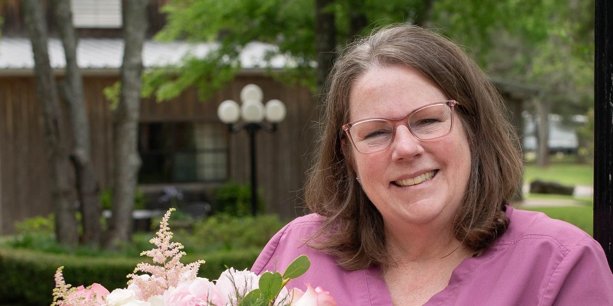 Smiling woman in glasses holding a bouquet of flowers outdoors.