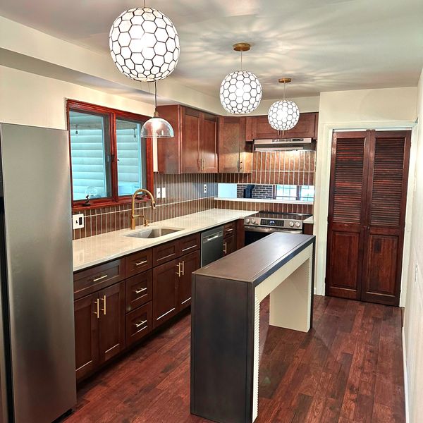Modern kitchen with dark wood cabinets, white countertops, and unique pendant lights.