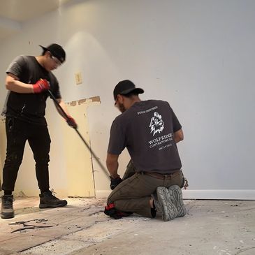 Two men removing flooring in a room under renovation.
