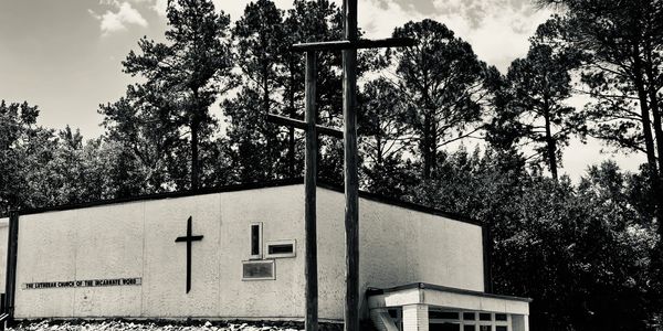 Black and white photo of a church with crosses and trees in the background.