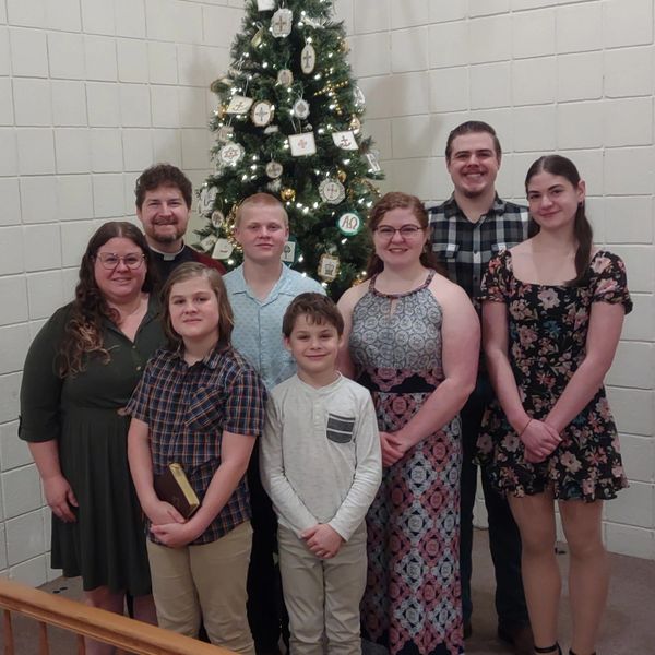 A smiling family of eight poses before a decorated Christmas tree indoors.