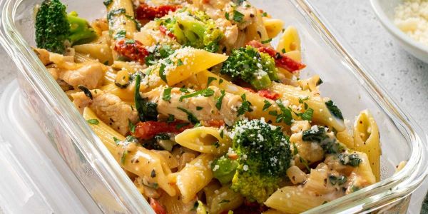 Pasta with chicken, broccoli, and sun-dried tomatoes in a glass dish.
