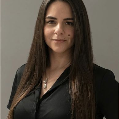 Young woman with long dark hair smiling gently, wearing a black top and cross necklace.