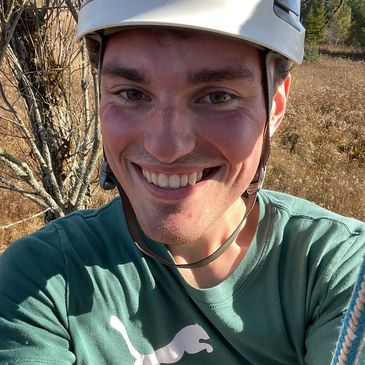 Smiling young man wearing a safety helmet outdoors in a natural setting.