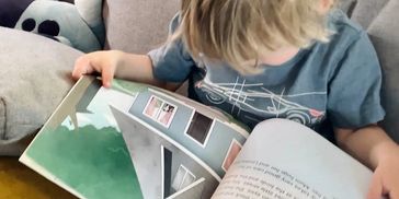 A young child reading a picture book on a couch.