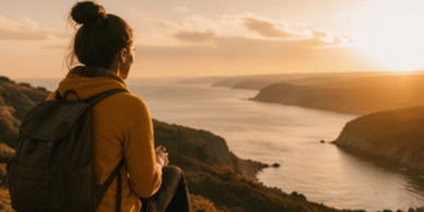 Person with backpack watching sunset over cliffs and water.