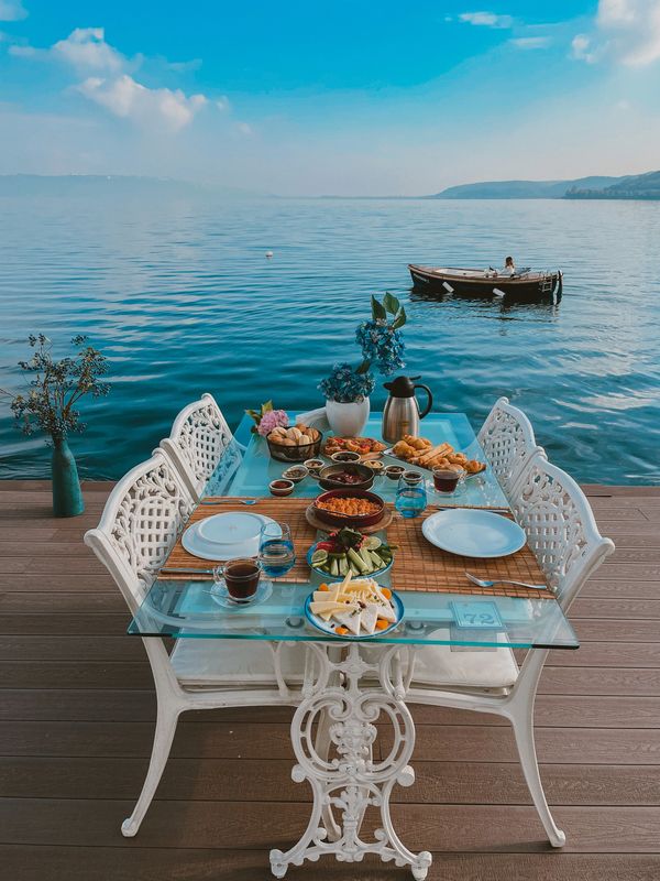 İskelede göl kenarında kurulmuş bir kahvaltı sofrası. Arkadan küçük ahşap bir tekne geçiyor