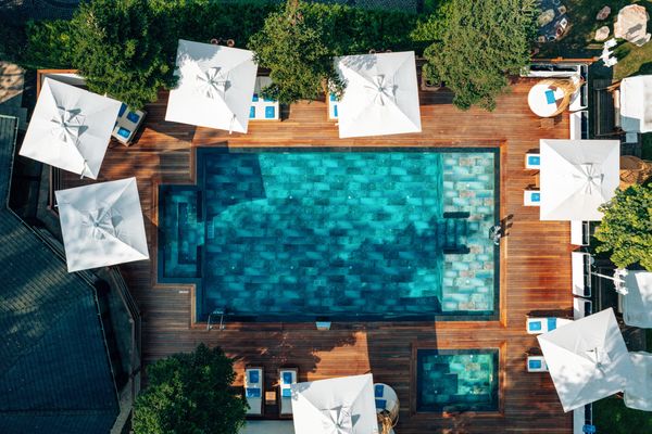 Tepeden açık havuz görüntüsü, ahşap deckler, beyaz şemsiyeler ve ahşap şezlonglar