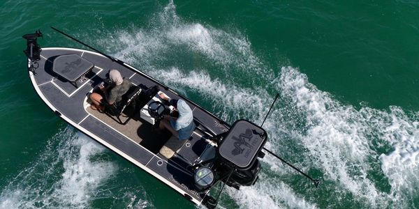 Two people fishing on a small boat in clear green water.