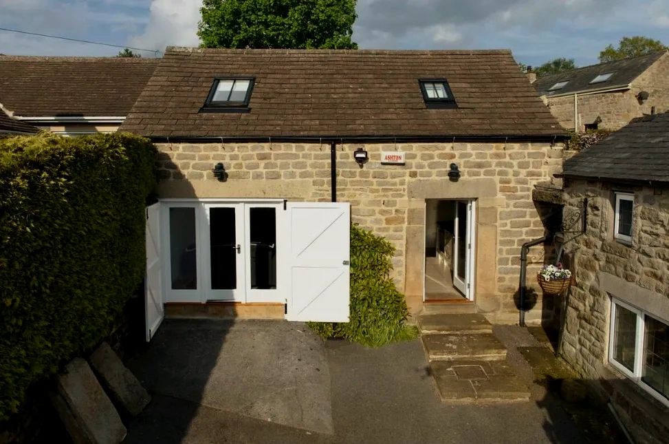 Stone cottage with white doors and windows under a cloudy sky.