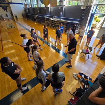 Coach giving a pep talk to volleyball players in a gym.
