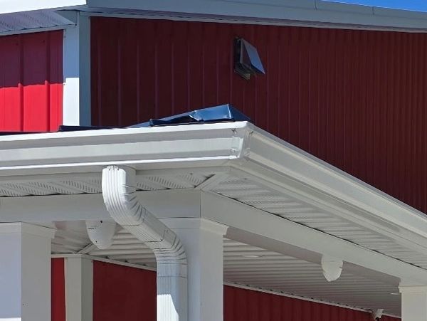 Close-up of a white roof gutter and downspout on a red building.
