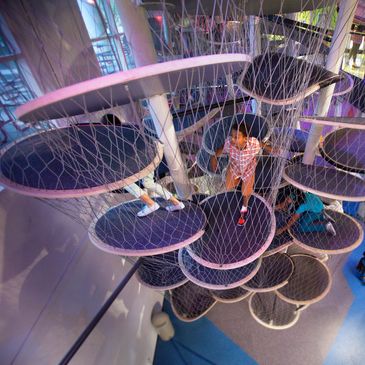 Children climbing through circular platforms surrounded by nets.