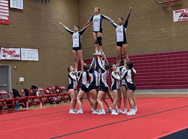 Cheerleaders performing a pyramid stunt in a gymnasium.