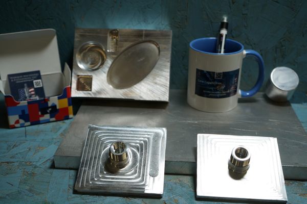 Metal plates with threaded inserts and a mug holding a pen on a workbench.