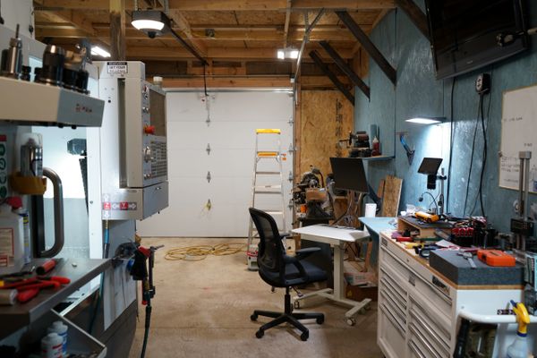 Organized workshop with tools, a computer, and a chair under wooden beams.