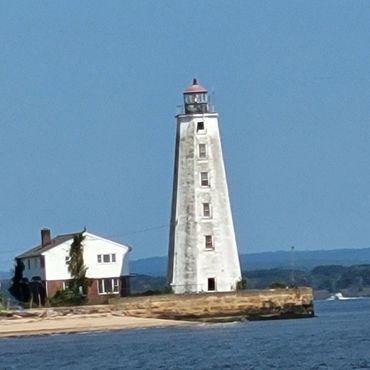 A tall white lighthouse near a small house on a coastal shore.