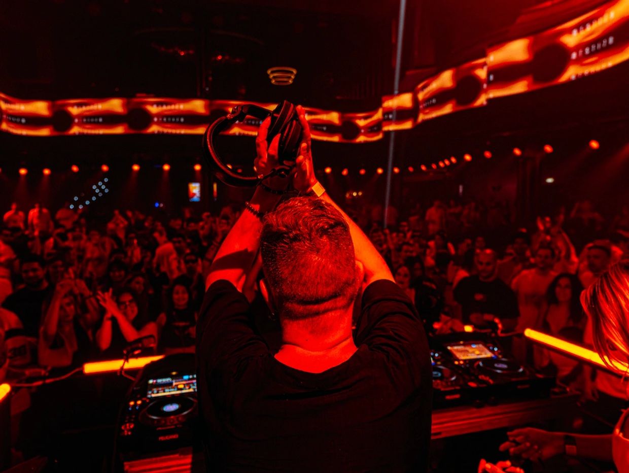 DJ cantando frente a una audiencia animada en luces rojas.
