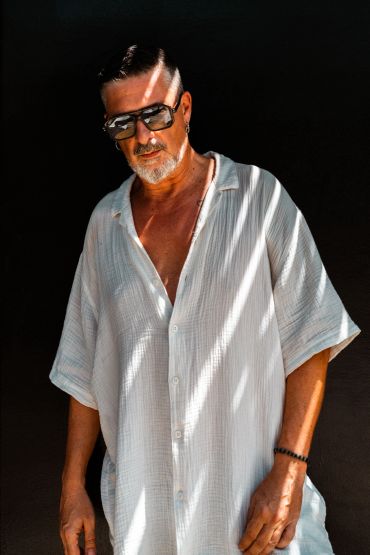 Hombre con camisa blanca y gafas oscuras bajo luz con sombras.