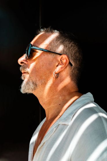 Hombre de perfil con gafas de sol y luz en rayas.