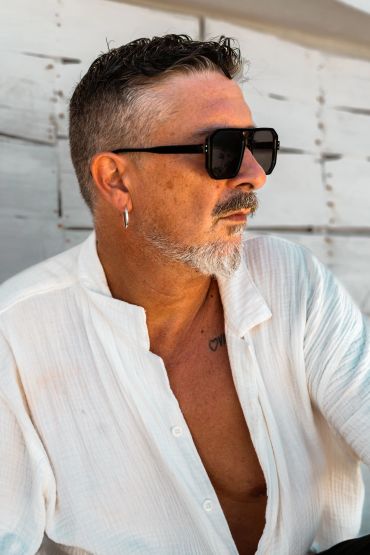 Hombre con gafas de sol y camisa blanca mirando al horizonte.