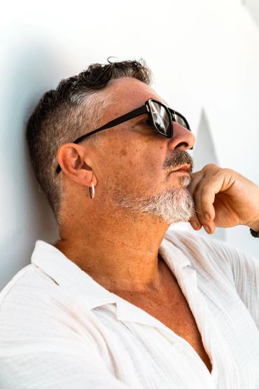 Hombre pensativo con gafas de sol y camisa blanca.