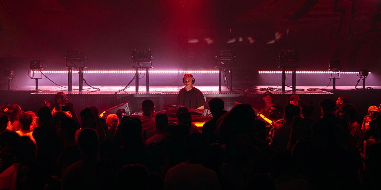 DJ tocando en una fiesta con luces rojas y público.