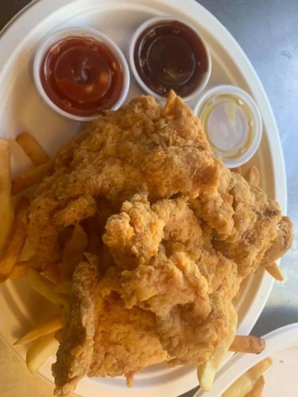 Fried chicken strips with fries and dipping sauces on a plate.