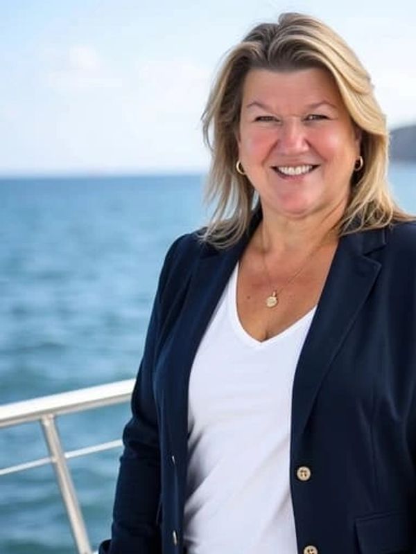 Smiling woman in a navy blazer by the sea on a sunny day.
