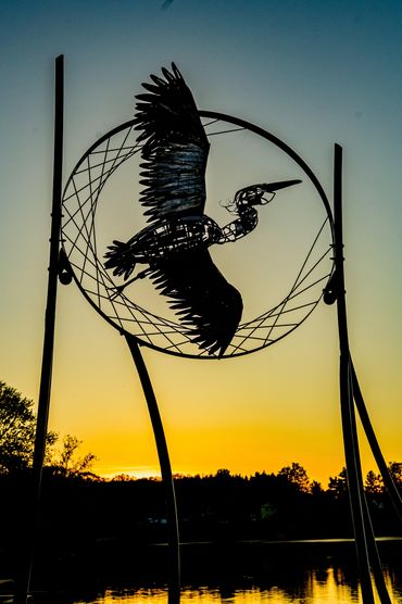 Silhouette of a bird sculpture against a sunset sky.