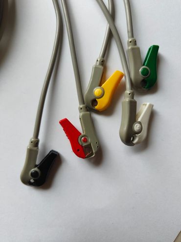 Colored alligator clips attached to gray wires on a white surface.