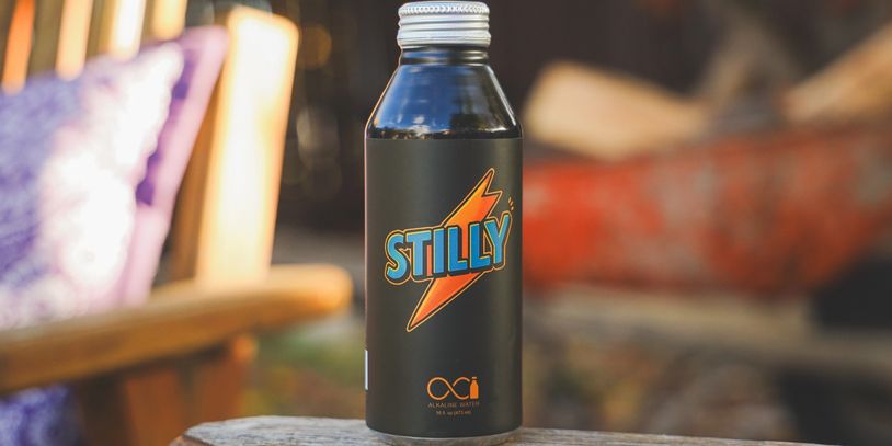 An aluminum bottle of alkaline water, in an outdoor setting with a nature backdrop 