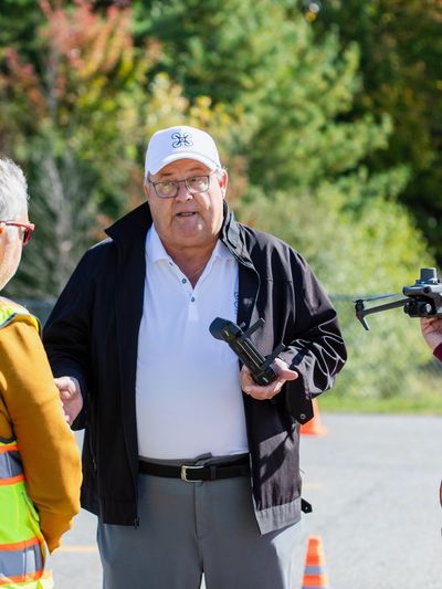 Man in white cap and black jacket holding a drone controller outdoors.