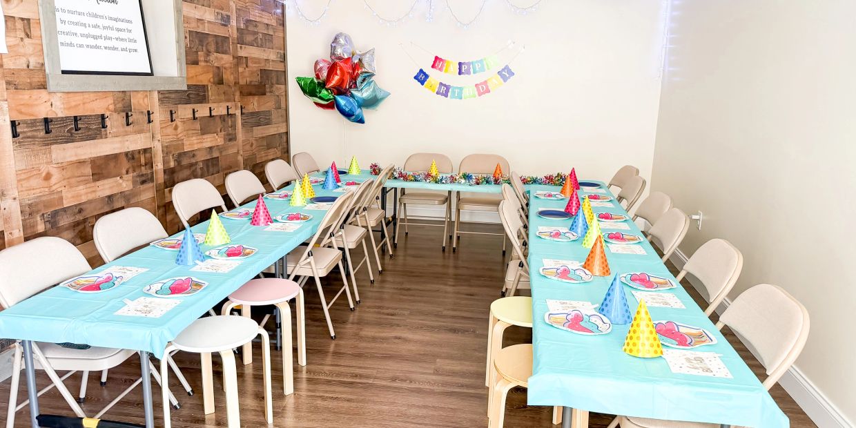 Colorful birthday party setup with tables, chairs, party hats, and balloons.
