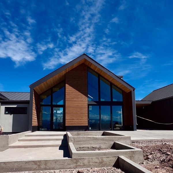 Modern house with large glass windows and wooden accents under a bright blue sky.