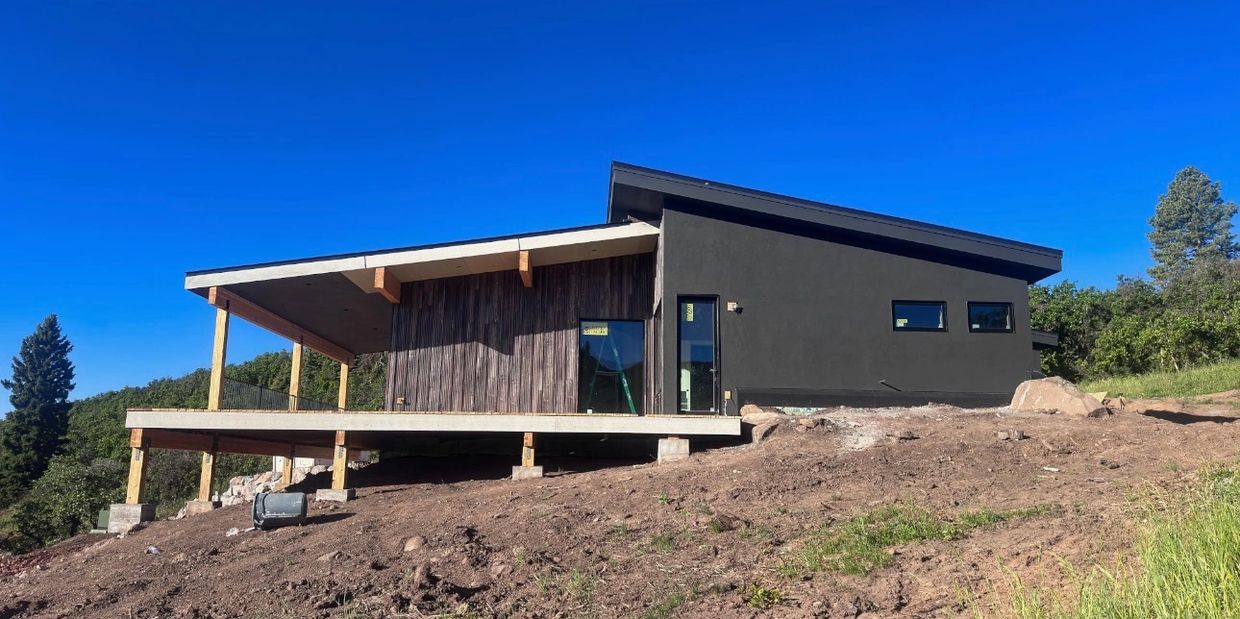 Modern house with dark exterior and large porch on a hillside.