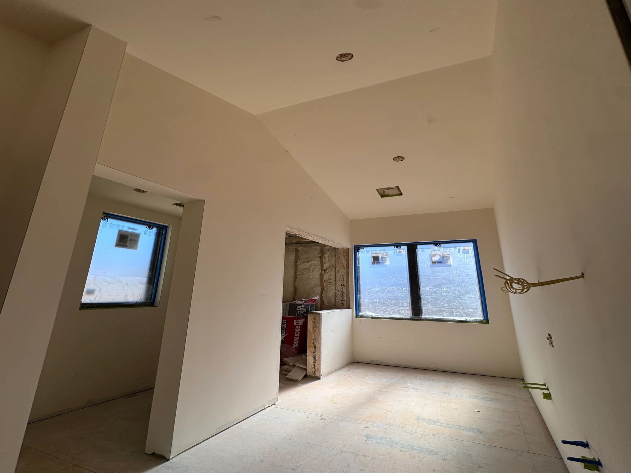 Interior of an unfinished room with large windows and white walls.