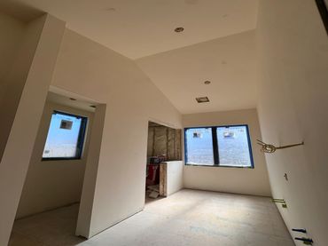 Interior of an unfinished room with large windows and white walls.
