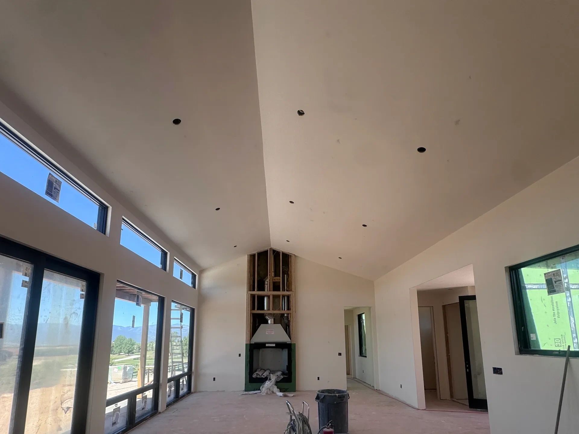 Spacious room under construction with vaulted ceiling and large windows.