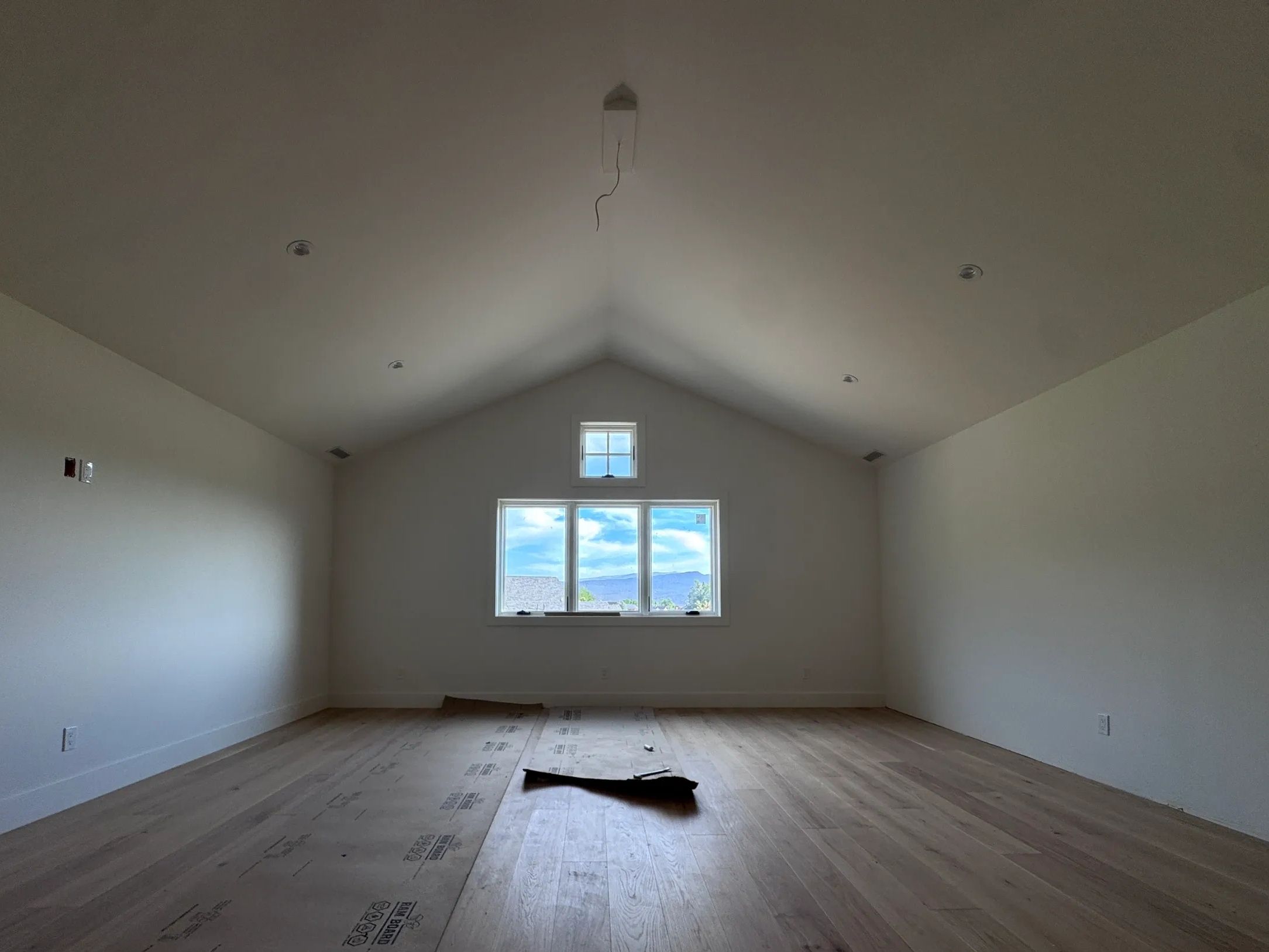 Empty room with wooden floor and a window showing a cloudy sky.
