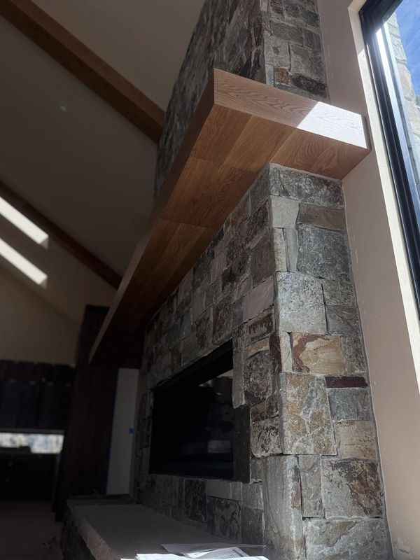 Stone fireplace with a wooden mantel near a large window.