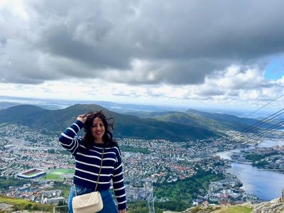 Woman posing on a mountain with a scenic city and lake view behind her.