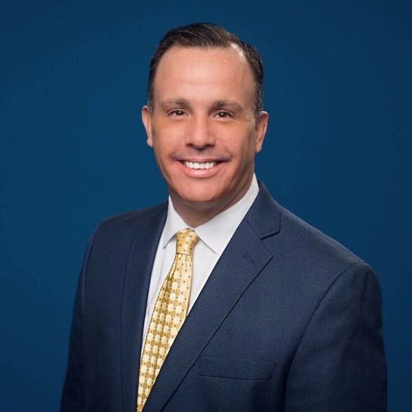 Professional man in a suit smiling against a blue background.