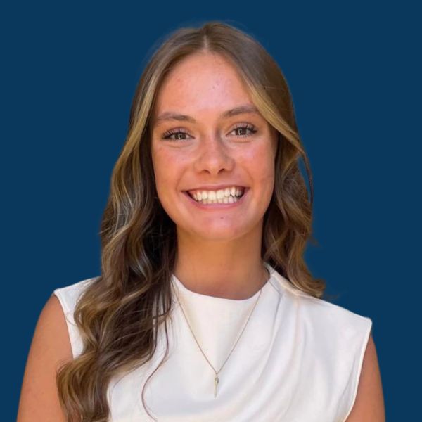 Young woman with wavy hair smiles against a blue background.