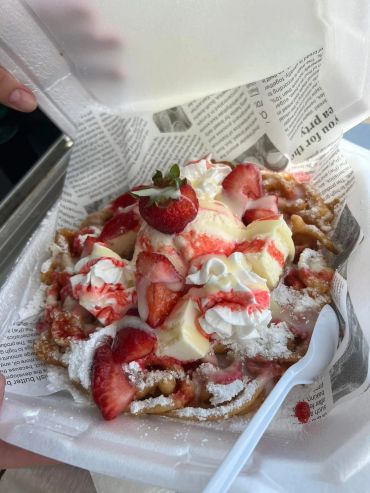 Funnel cake topped with strawberries, whipped cream, and powdered sugar.