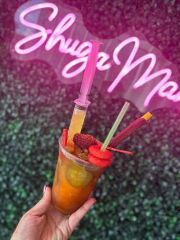 Colorful drink with a pink syringe and garnishes.