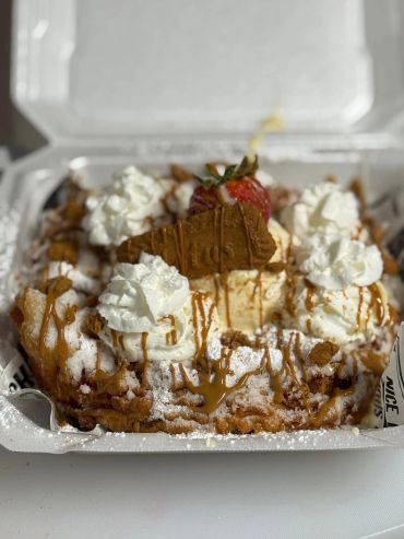 Funnel cake with whipped cream, caramel drizzle, a strawberry, and cookie.