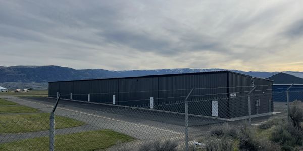 Large dark hangar behind chain-link fence with mountains in background.