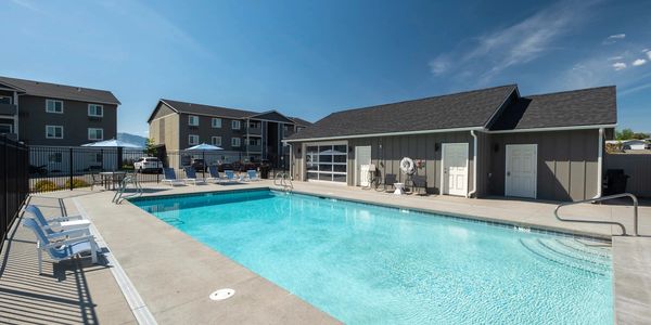 Outdoor swimming pool area with lounge chairs and apartment buildings in the background.
